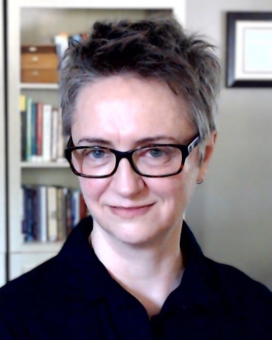 Closeup photo of a person wearing a black collared shirt, with short hair, wearing eyeglasses, and smiling at the camera. 